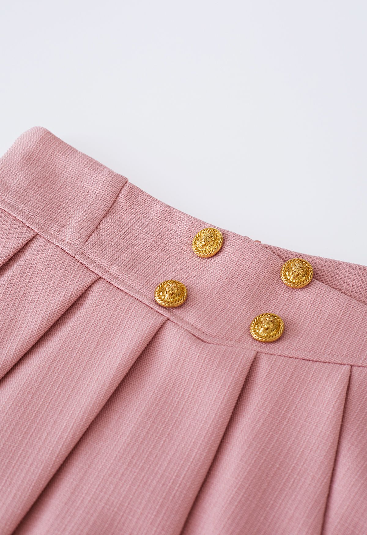 تنورة قصيرة مطوية بأزرار ذهبية باللون الوردي